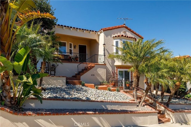 mediterranean / spanish home featuring stairs, a tiled roof, a porch, and stucco siding