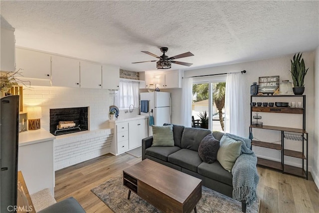 living area with plenty of natural light, light wood finished floors, a textured ceiling, and a brick fireplace