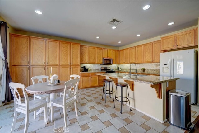 kitchen with visible vents, a breakfast bar, an island with sink, a sink, and stainless steel appliances