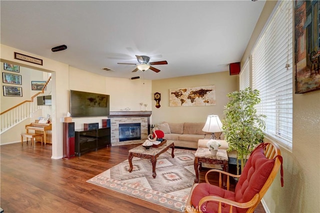 living area with stairway, wood finished floors, visible vents, a ceiling fan, and a stone fireplace