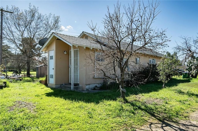 view of property exterior with roof with shingles, a lawn, and stucco siding