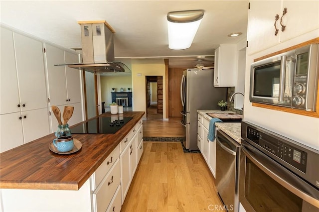 kitchen with island range hood, butcher block counters, light wood-style flooring, stainless steel appliances, and white cabinetry