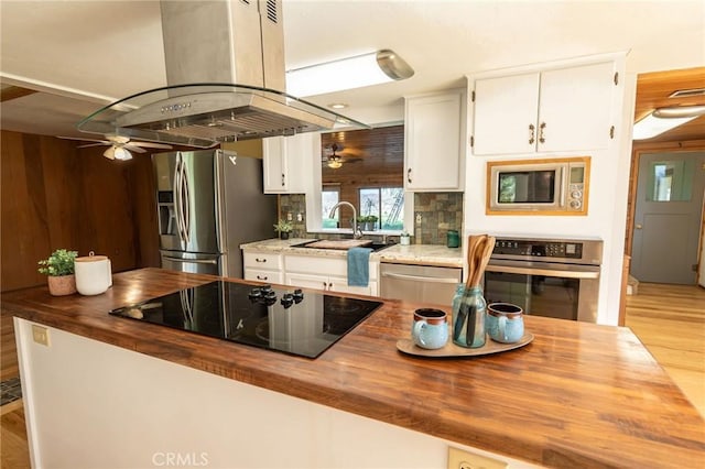 kitchen with wooden counters, appliances with stainless steel finishes, white cabinets, a sink, and island range hood