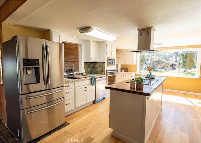 kitchen with decorative backsplash, appliances with stainless steel finishes, white cabinets, a sink, and island range hood