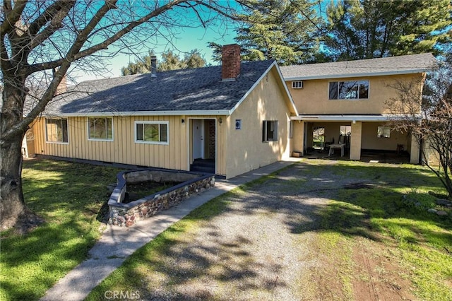 view of front of property with a shingled roof, driveway, a chimney, and a front lawn