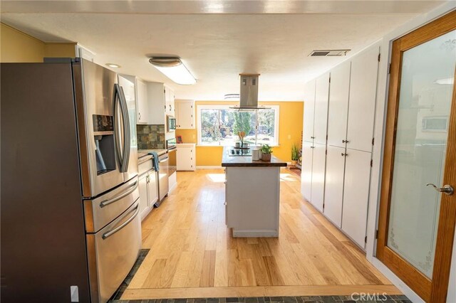 kitchen with light wood-style flooring, island range hood, visible vents, appliances with stainless steel finishes, and tasteful backsplash