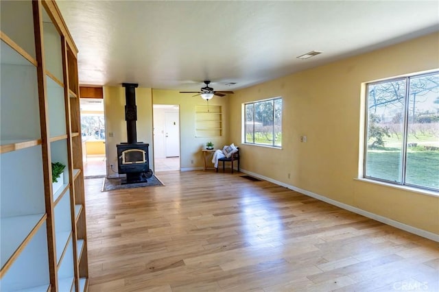 unfurnished living room featuring a wood stove, light wood-style flooring, visible vents, and baseboards