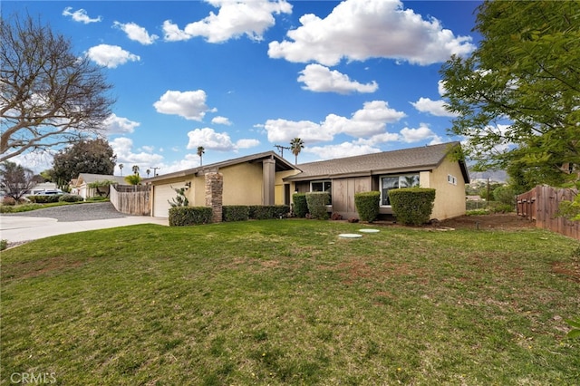 view of front facade with fence, a front yard, stucco siding, a garage, and driveway