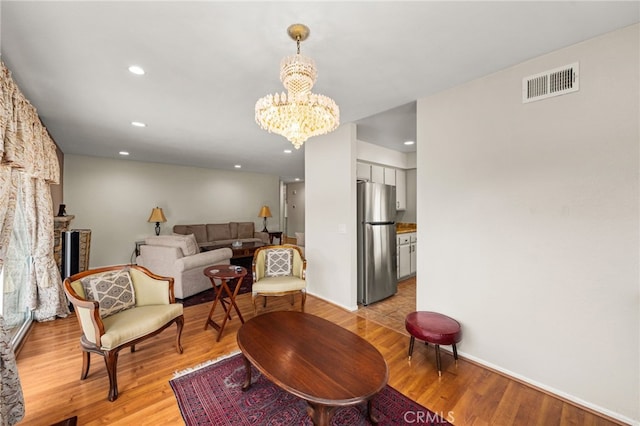 living area with light wood finished floors, visible vents, recessed lighting, and an inviting chandelier