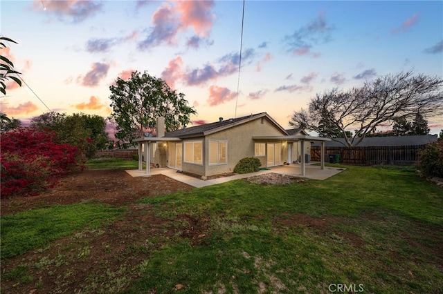 back of property at dusk with a fenced backyard, stucco siding, a yard, and a patio