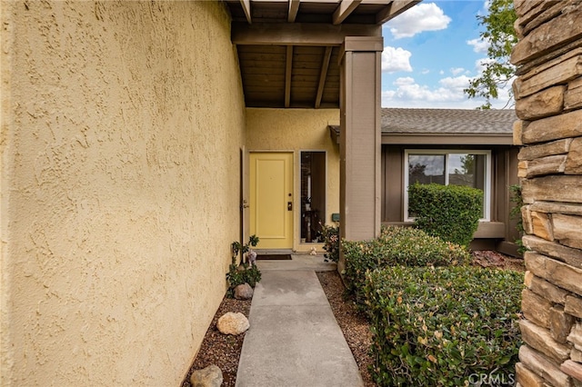 doorway to property featuring roof with shingles and stucco siding