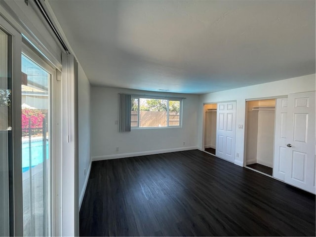 unfurnished bedroom featuring dark wood-style floors, baseboards, and two closets