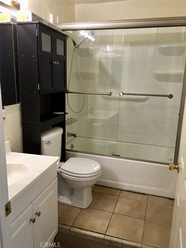 bathroom featuring toilet, tile patterned flooring, combined bath / shower with glass door, and vanity