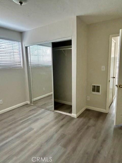 unfurnished bedroom with multiple windows, wood finished floors, visible vents, and baseboards