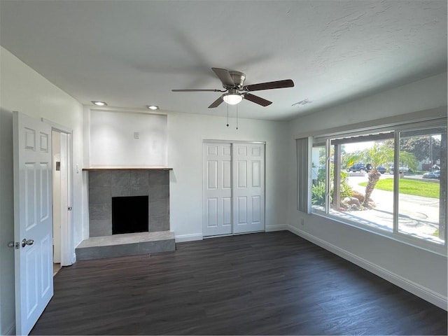 unfurnished living room with a fireplace, a ceiling fan, visible vents, baseboards, and dark wood finished floors