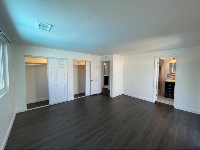 unfurnished bedroom featuring baseboards, visible vents, dark wood-style flooring, and ensuite bathroom