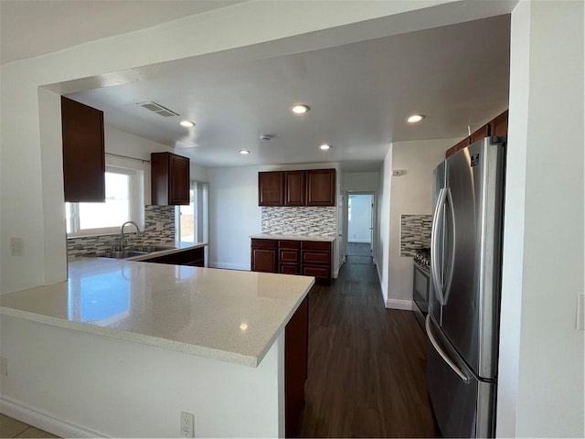 kitchen with visible vents, dark wood-type flooring, freestanding refrigerator, a peninsula, and a sink