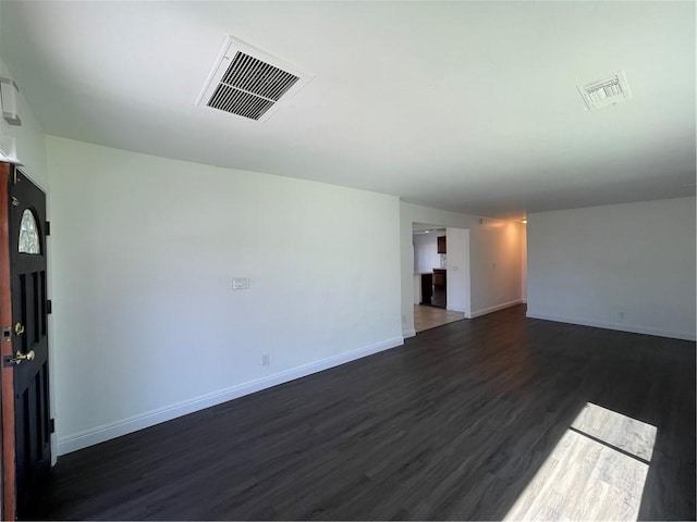 unfurnished room featuring dark wood finished floors, visible vents, and baseboards