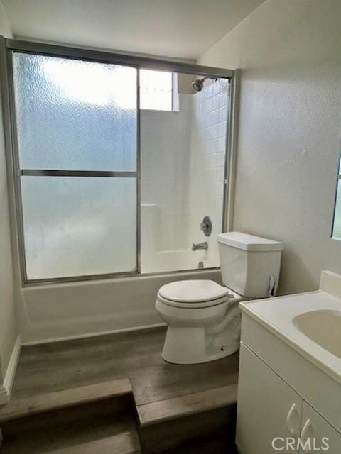 bathroom featuring toilet, combined bath / shower with glass door, wood finished floors, and vanity