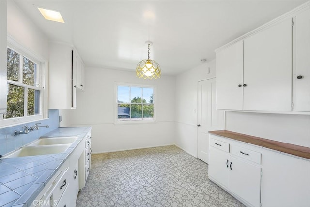 kitchen featuring a sink, tile counters, white cabinets, and hanging light fixtures