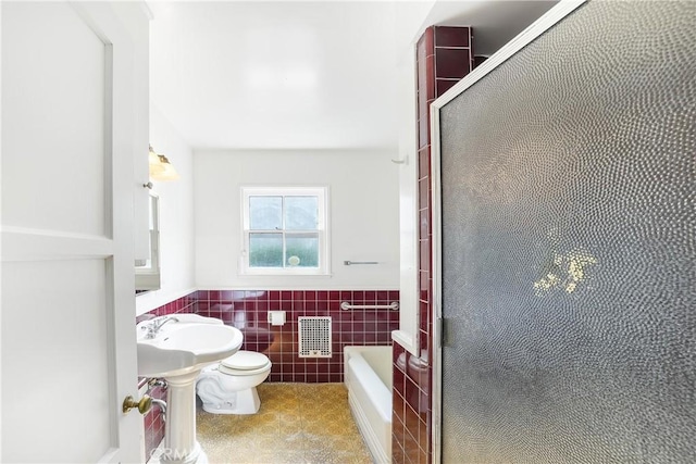 full bathroom with a tub, a wainscoted wall, toilet, a shower with shower door, and tile walls