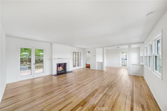 unfurnished living room featuring a fireplace with flush hearth, light wood-style floors, and french doors