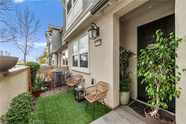 doorway to property with fence, central AC unit, and stucco siding