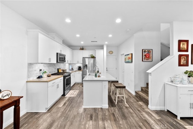 kitchen featuring tasteful backsplash, a center island with sink, appliances with stainless steel finishes, a breakfast bar, and wood finished floors