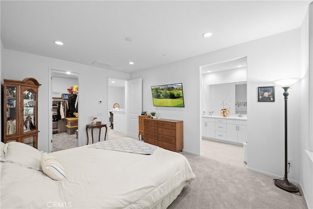 bedroom with light carpet, ensuite bathroom, a walk in closet, a closet, and recessed lighting