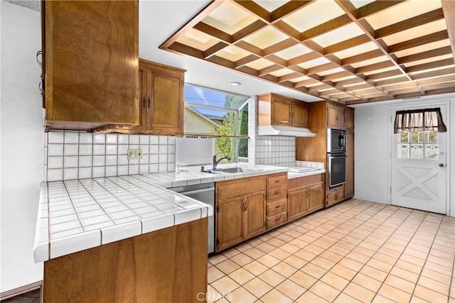 kitchen featuring a sink, tasteful backsplash, coffered ceiling, appliances with stainless steel finishes, and tile counters