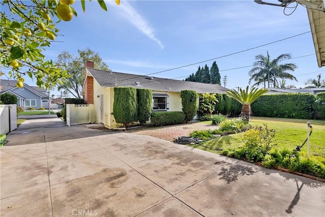 view of front of house with a chimney, stucco siding, concrete driveway, and a front lawn