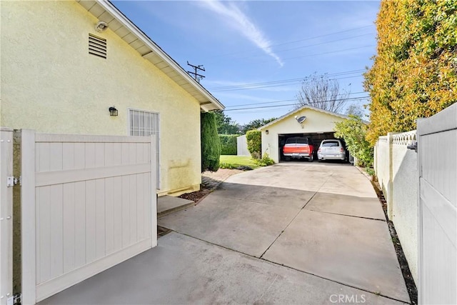 view of property exterior with stucco siding, a detached garage, an outdoor structure, and fence