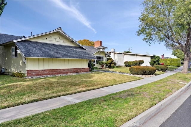 view of front of house featuring brick siding, a front yard, and roof with shingles