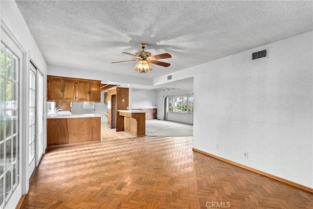 kitchen with visible vents, brown cabinets, open floor plan, a peninsula, and light countertops