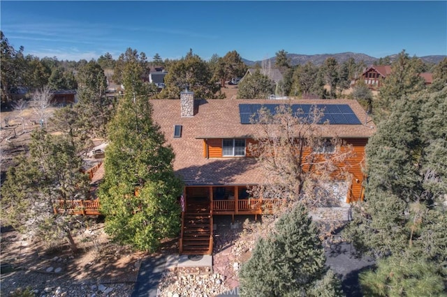 back of house with a chimney, roof with shingles, a deck with mountain view, stairs, and roof mounted solar panels