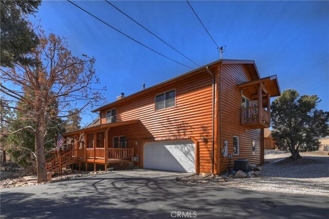 view of home's exterior featuring driveway, a garage, log veneer siding, a balcony, and cooling unit