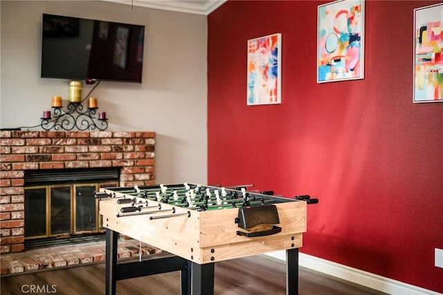 rec room featuring crown molding, a fireplace, wood finished floors, and baseboards