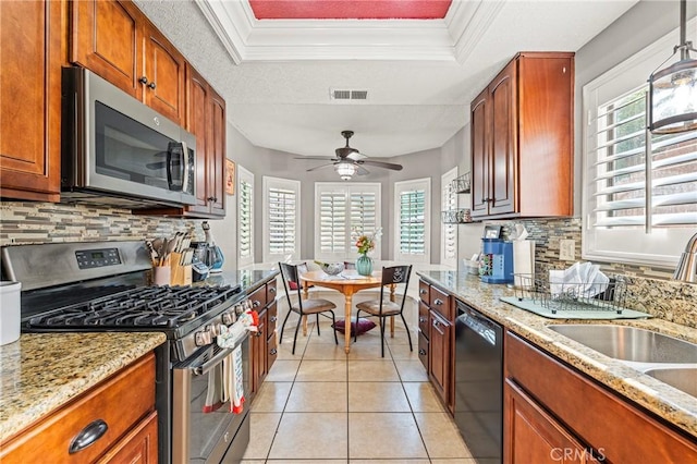 kitchen with light tile patterned flooring, stainless steel appliances, visible vents, ornamental molding, and a raised ceiling