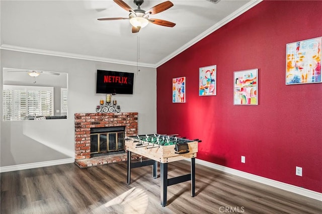 game room featuring a brick fireplace, crown molding, baseboards, and wood finished floors