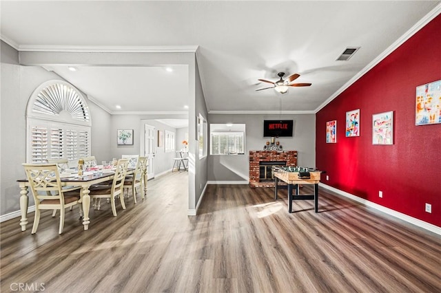 dining area featuring a fireplace, wood finished floors, a ceiling fan, baseboards, and crown molding