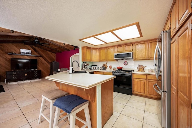 kitchen featuring wooden walls, appliances with stainless steel finishes, a kitchen bar, a sink, and light tile patterned flooring