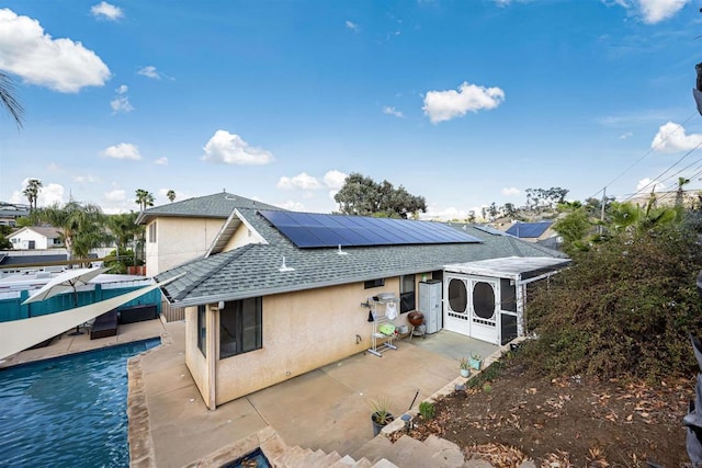 back of house with a shingled roof, an outdoor pool, a patio, roof mounted solar panels, and stucco siding