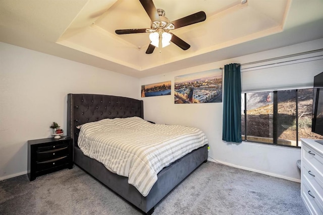 carpeted bedroom with ceiling fan, baseboards, and a raised ceiling