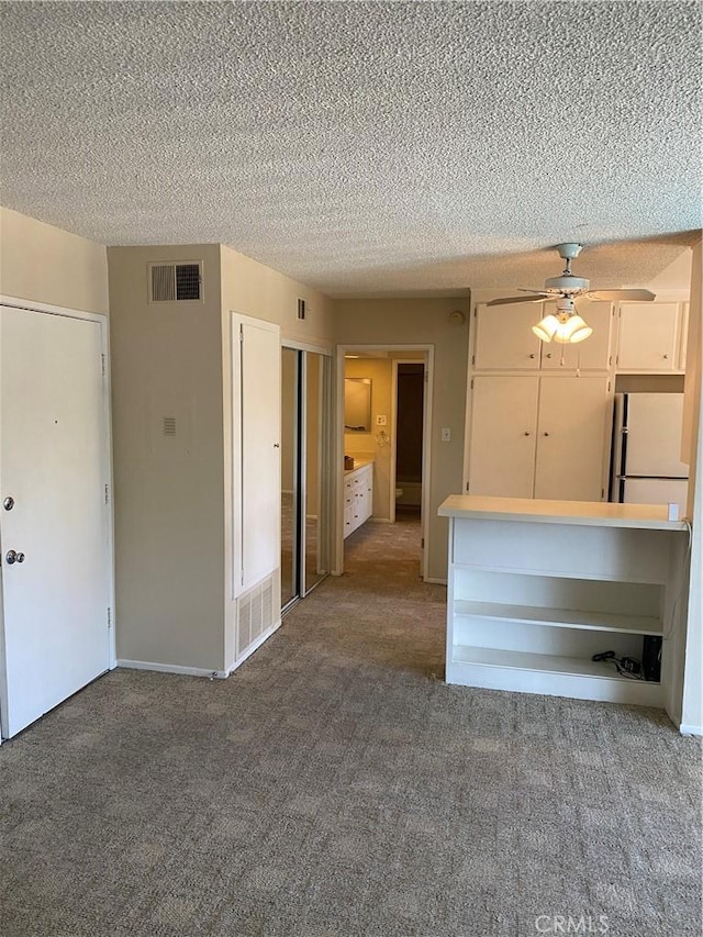 unfurnished living room featuring a textured ceiling, carpet flooring, visible vents, and a ceiling fan