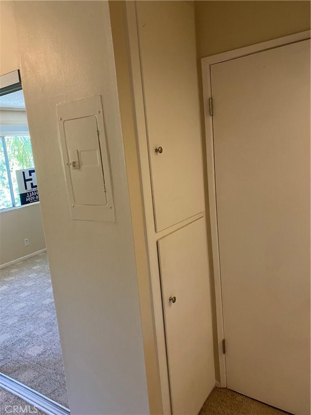 hallway featuring electric panel and light carpet