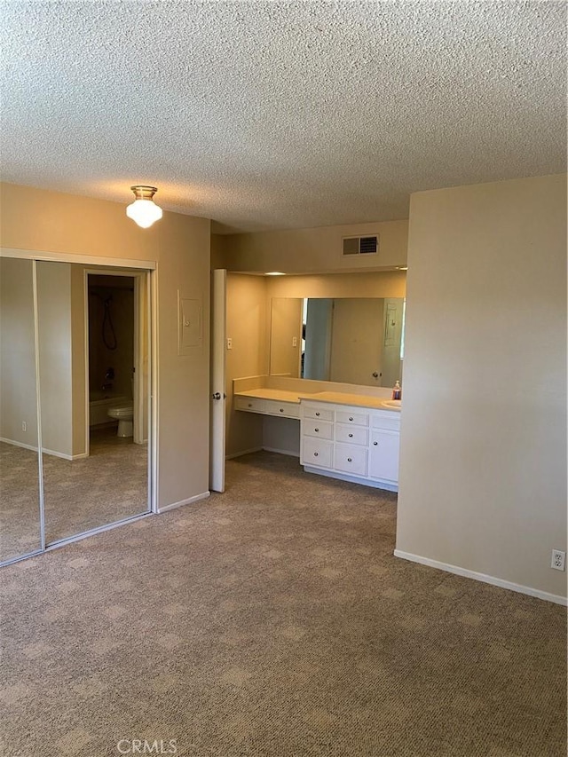 unfurnished bedroom featuring baseboards, visible vents, dark colored carpet, built in desk, and a closet