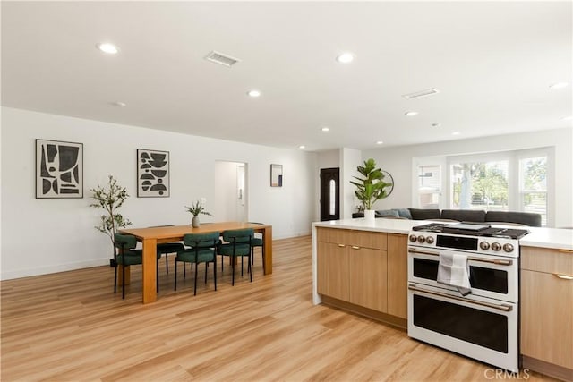 kitchen with double oven range, visible vents, light wood finished floors, light brown cabinetry, and modern cabinets