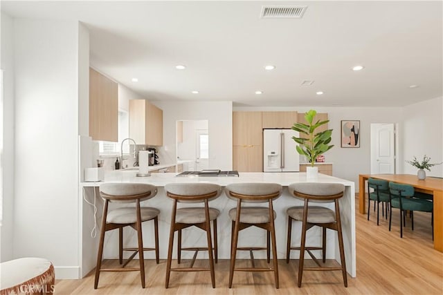 kitchen featuring visible vents, white fridge with ice dispenser, a peninsula, a breakfast bar area, and light countertops