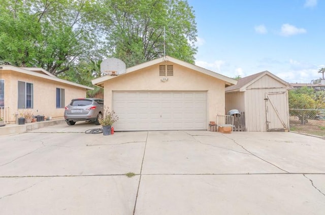 view of front facade with a garage, concrete driveway, fence, an outdoor structure, and stucco siding