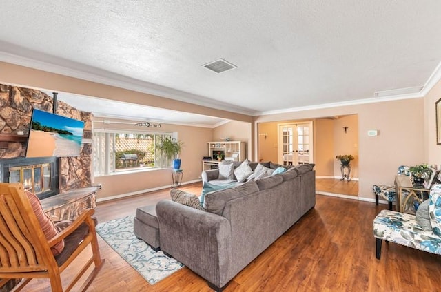 living area with a textured ceiling, a fireplace, wood finished floors, ornamental molding, and french doors